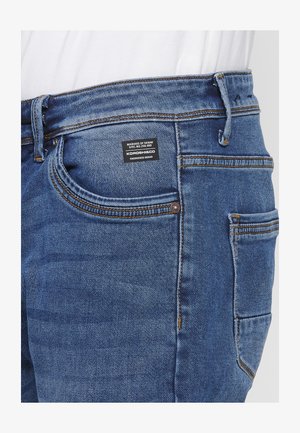 Blauwe denim jeans met een klassiek vijf-pocket ontwerp, contrasterende stiksels en een merklabel op de achterste tailleband. Gekozen textuur.