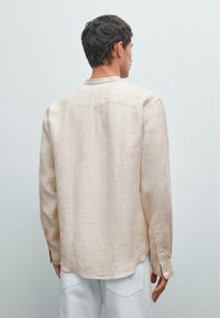 Beige Langarmhemd aus leicht strukturiertem Stoff. Dezente vertikale Streifen, gerade Saum und geknöpfte Manschetten. Einfaches Design, Rückansicht.