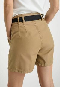 Shorts kaki avec une texture douce, dotés d'une ceinture élastique noire et de poches latérales inclinées, se terminant au-dessus du genou.