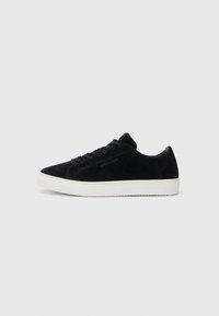 Adidași din suede negru, cu un design low-top, vârf rotund și talpă din cauciuc alb. Prezintă sireturi negre și un branding minim pe lateral.