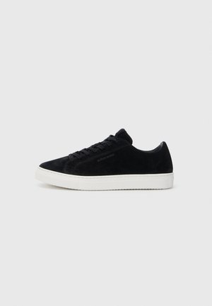 Sneaker in suede nera con design a low-top, punta tonda e suola in gomma bianca. Presenta lacci neri e un branding minimale sul lato.
