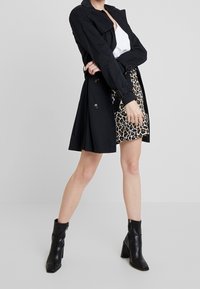 Abrigo negro de trench con cintura ceñida, combinado con una falda de estampado de leopardo. Botines negros con tacón grueso. Textura de tela suave.
