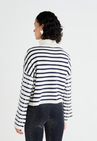 Striped sweater with a high neckline, featuring navy blue and white horizontal stripes and sequined accents on sleeves. Cropped design.