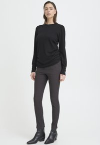 Black long-sleeve top with gathered side detail paired with fitted dark patterned trousers and ankle boots. Smooth texture, simple design.