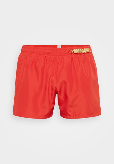 Shorts de bain rouges en matériau léger et lisse. Dotés d'une taille élastique et d'un élément décoratif en or sur le devant.