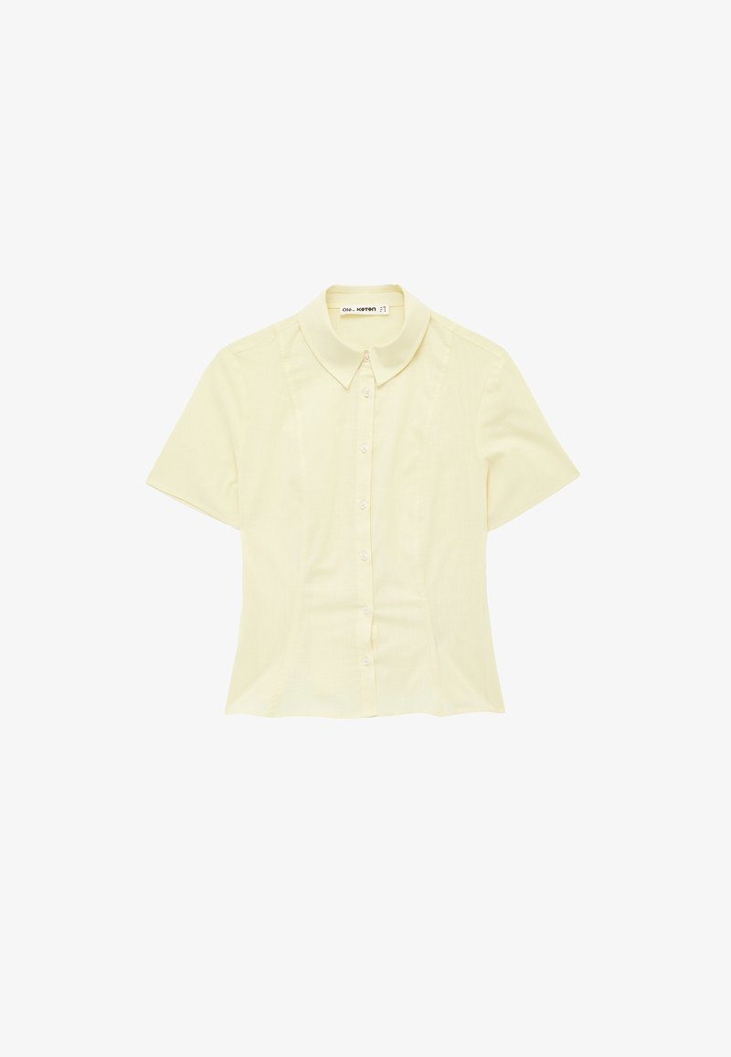 Blouse jaune pâle à manches courtes, boutonnée, avec col pointu et taille cintrée.