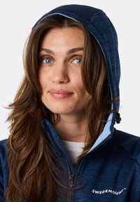 Marineblauer Reißverschluss-Hoodie mit Kapuze, ausgestattet mit einem hellblauen Innenfutter und strukturiertem Stoff. Logo auf der Vorderseite rechts sichtbar.