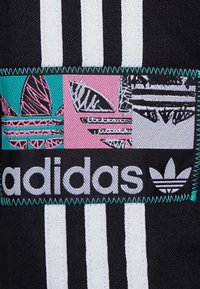 Musta kangas, jossa on kolme valkoista pystysuoraa raitaa ja monivärinen brodeerattu Adidas-logo, jossa on turkoosin, vaaleanpunaisen ja mustan elementtejä.