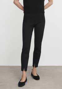 Pantalons noirs ajustés avec une coupe slim, dotés d'une fente sur le bas. Fabriqués dans un tissu lisse, offrant une silhouette élégante.