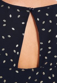 Robe de marine avec des motifs épars ressemblant à des feuilles d'or, dotée d'une ouverture en clé au dos fermée par un bouton foncé. Tissu lisse et léger.