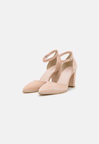 Beige suede high-heeled shoes with pointed toes and an ankle strap. Features a textured finish and a block heel for stability.