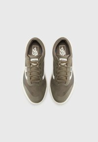 Baskets vert olive avec dessus en mesh et tissu, accents blancs, lacets plats et semelle rembourrée. Logo de marque notable sur la languette.