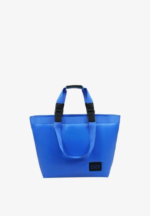 Blå tote bag lavet af slidstærkt materiale, med to solide stropper, sorte hardware-detaljer og en rektangulær form. Logo på forsiden.