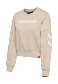Beige crewneck sweatshirt with long sleeves, white "HUMMEL" text on front, white chevron stripes on sleeves, and red tag near hem.