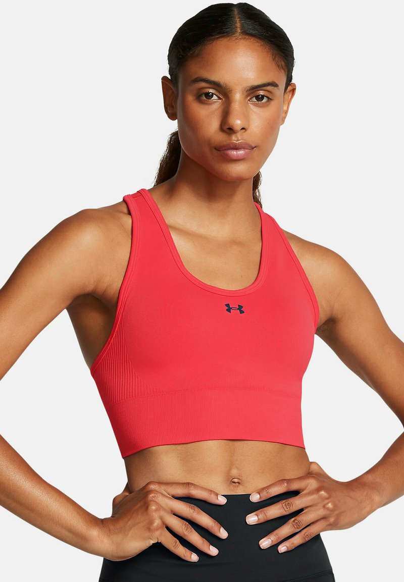 Sarkans sporta krūšturis ar ribotu tekstūru un noapaļotu kakla izgriezumu. Centrā uz krūtīm atrodas Under Armour logo tumši zilā krāsā.