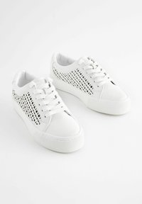 Sneakers bianchi con lati in pelle perforata, lacci piatti e una suola spessa e testurizzata. Design pulito con dettagli hardware minimi.