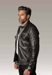 Veste en cuir marron pour moto avec des accents matelassés aux épaules, des zips sur les côtés et un col montant. Présente une texture lisse et un design classique.