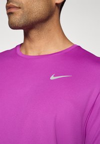 Lilla Nike T-shirt med rund halsudskæring og korte ærmer, udstyret med et lille sølvlogo på venstre bryst. Glat, struktureret stof.