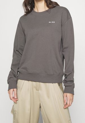 Felpa grigia con collo rotondo, maniche lunghe, polsini e orlo a coste, caratterizzata da un piccolo logo bianco sul petto, abbinata a pantaloni beige a gamba larga.