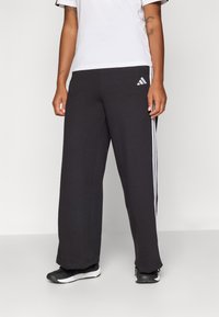 Pantaloni sportivi negri din material jersey, cu dungi albe pe laterale, picioare largi și un brâu elastic pentru confort.