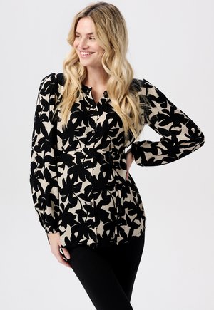 Schwarze und beigefarbene Bluse mit floralem Muster, langen Ärmeln, Knopfverschluss und taillierter Passform, kombiniert mit schwarzen Leggings.