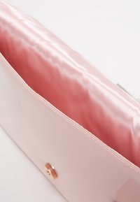 Pochette en cuir verni rose avec un extérieur lisse et brillant ; elle possède un intérieur en satin rose doux et une fermeture à pression en or rose.