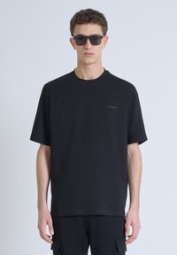 T-shirt nera a maniche corte con scollo rotondo, con un piccolo logo grigio sul lato sinistro del petto, realizzata in un tessuto liscio e traspirante.