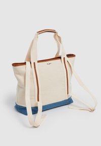 Plátěná taška v krémové barvě s modrým dnem. Disponuje hnědými koženými detaily a dlouhými popruhy, navržena pro pohodlné nošení.