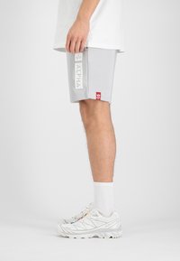 Shorts de sport gris en tissu doux avec un grand imprimé "ALPHA" sur le côté et un petit patch logo rouge à l'ourlet.