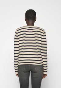 Neulepusero, jossa on kerma- ja laivastonsinisiä vaakasuoria raitoja, pyöreä kaula-aukko ja pitkät hihat. Kangas vaikuttaa teksturoidulta ja ribatulta.