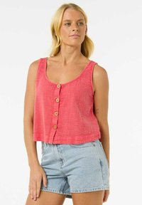Top corto de color coral con un acabado texturizado, que presenta un escote redondeado y cinco botones de madera en el frente. Combinado con shorts de mezclilla claros.