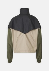 Färgblockad jacka med en svart överdel, khaki mitten och gröna ärmar. Tillverkad av ett mjukt, lätt material med hög krage.