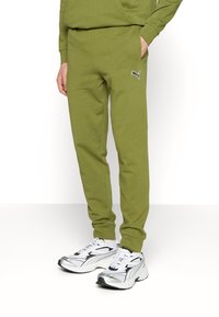 Olivgröna bomullssweatpants med en tapered fit, sidofickor och en liten vit Puma-logotyp på vänster sida. Bärs med vita och svarta sneakers.