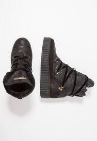 Mustat korkeavartiset tennarit, jotka on valmistettu tekstuuripinnoitteisesta nahasta ja mokkasuedeista. Kenkien sisällä on tekoturkki, ja ne on varustettu nauhakiinnityksellä sekä kultaisilla yksityiskohdilla.