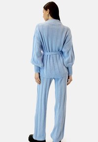 Jasnoniebieski zestaw dzianinowy składający się z kardiganu z paskiem i długimi rękawami oraz pasujących spodni. Miękka faktura z pionowymi paskami.