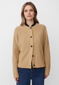 Beige gestrickte Strickjacke mit rundem Halsausschnitt, Knopfverschluss und geripptem Saum. Schwarze Knöpfe stehen im Kontrast zum weichen Material.
