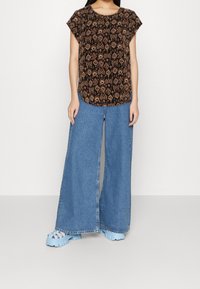 Svart mönstrad topp med korta ärmar, kombinerad med vida blå jeansbyxor. Outfitten fulländas med kraftiga ljusblå skor.