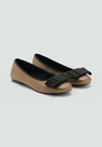 Un paio di ballerine in bronzo con fodera interna nera e grandi fiocchi neri di tessuto sulla parte anteriore, esposte su uno sfondo grigio chiaro.