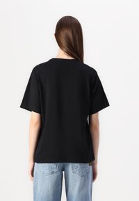 Černé bavlněné tričko s krátkým rukávem, kulatým výstřihem a uvolněným střihem. Měkká textura, minimalistický design, bez viditelných vzorů nebo grafik.