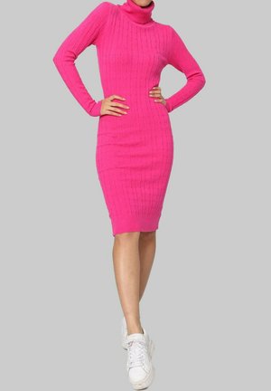 Robe tricotée rose ajustée avec un col montant, des manches longues et une longueur au genou. Portée avec des baskets blanches.