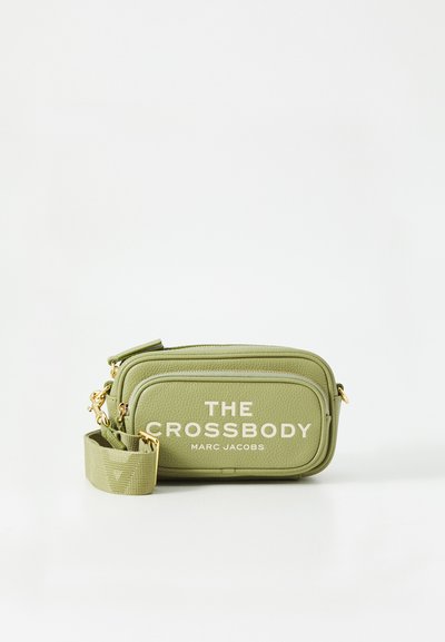 Groene crossbody tas van textuurmateriaal, met gouden hardware en gedurfde witte letters, ontworpen met een compacte, rechthoekige vorm.
