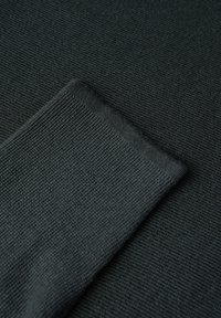 Tessuto grigio scuro che mostra una fine trama a coste, con un bordo piegato e una finitura liscia, che evidenzia il suo materiale morbido e il motivo uniforme.