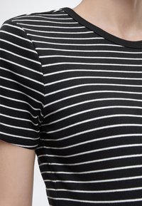 Μαύρο κοντομάνικο μπλουζάκι με ριγέ σχέδιο και λεπτές λευκές οριζόντιες ρίγες, που καλύπτει την περιοχή του άνω στήθους και των ώμων ενός ατόμου.