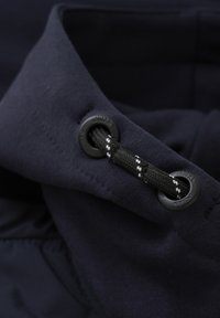 Marine tyg med en slät textur, som har ett svart ögla och ett flätat svart snöre med vita accenter för åtdragning. Nära bild.