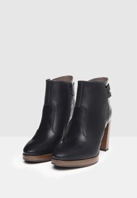 Botines de cuero negro con un acento texturizado de estampado de cocodrilo, cremallera lateral y tacón de madera. Punta redonda y detalles de hardware mínimos.