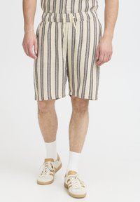 Striped shorts in beige and navy, featuring an elastic waistband with drawstrings. Paired with white socks and cream sneakers.