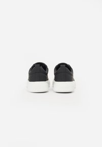 Baskets noires avec une tige en cuir lisse, semelle en caoutchouc blanc, col rembourré et design minimaliste. Pas de marquage visible à l'arrière.