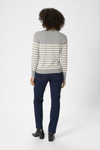 Un pull rayé gris et crème à manches longues, associé à un jean bleu foncé et des bottes à talons noires. Il possède un col rond et des poignets côtelés.