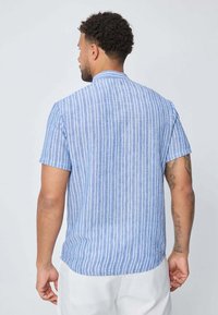 Chemise à manches courtes en bleu clair avec des rayures verticales blanches, dotée d'un col montant et d'une coupe décontractée. Texture similaire au lin et tissu doux.