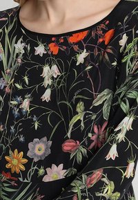 Svart tygtröja med ett livligt blommönster i olika färger, inklusive röd, gul och grön, dekorerad med intrikata mönster.